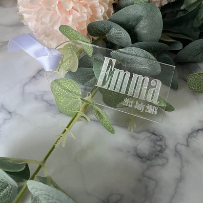 Clear Acrylic Luggage Tag wedding Place Card with 'Emma' and date on a marble surface with greenery
