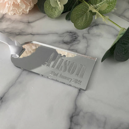 Silver Acrylic Luggage Tag wedding Place Card on a marble surface with flowers and leaves.