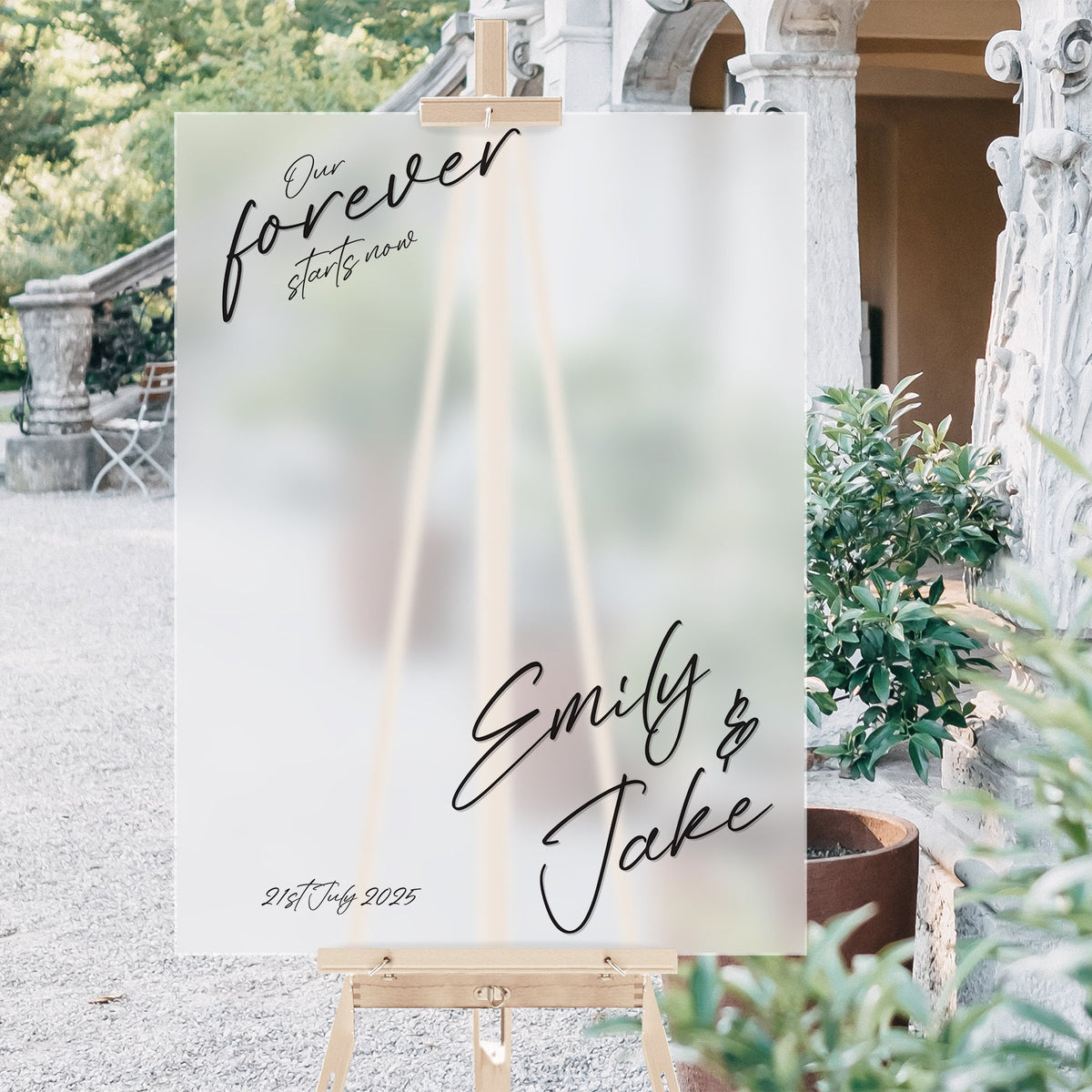 Wedding sign with 'Forever Starts Now' and names on an easel outdoors.