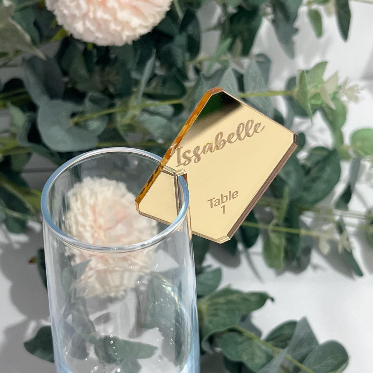 Gold name tag on a glass with flowers and greenery in the background