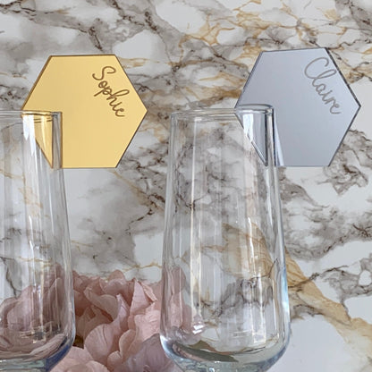 Two clear glass tumblers with gold and silver name tags on a marble surface.