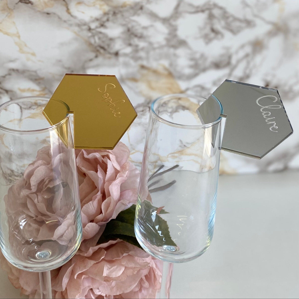 Two wine glasses with gold and silver place cards on a marble surface