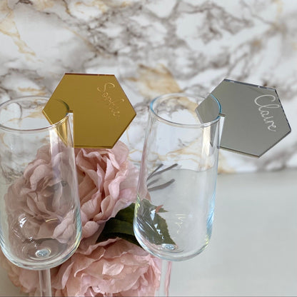 Two wine glasses with gold and silver place cards on a marble surface