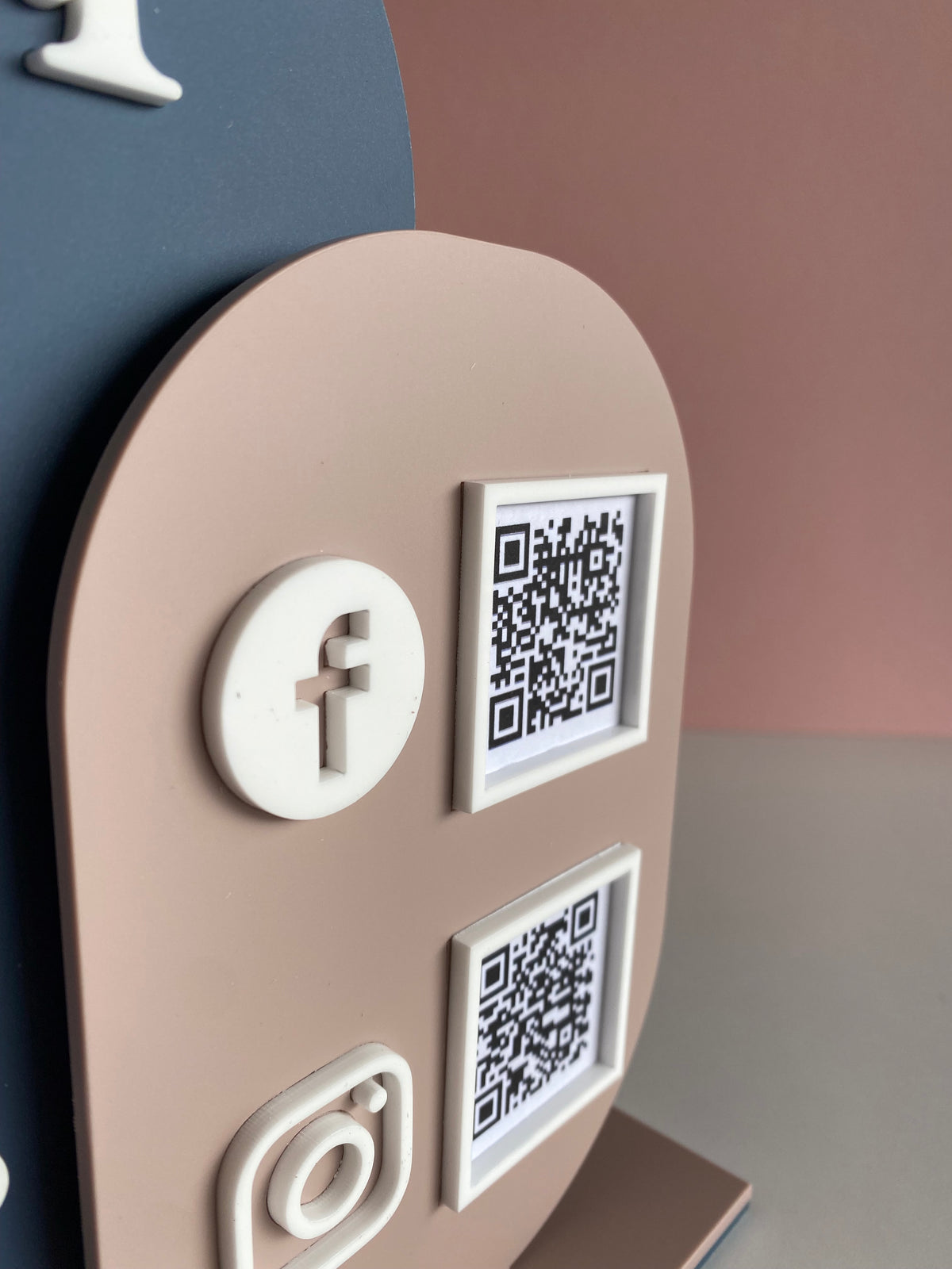 A double layer acrylic QR code sign free standing, with space for a logo and two QR codes, displayed on a white surface against a pink background.
