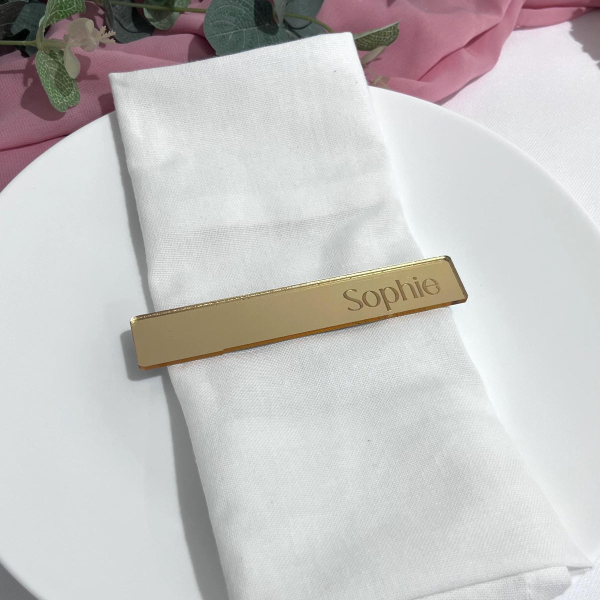Gold mirror acrylic Engraved Guest Name Card with 'Sophie' on a white napkin against a pink fabric background