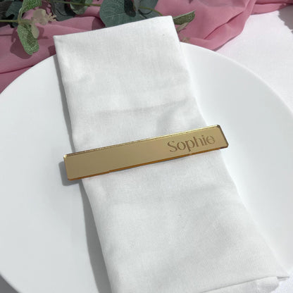 Gold mirror acrylic Engraved Guest Name Card with 'Sophie' on a white napkin against a pink fabric background