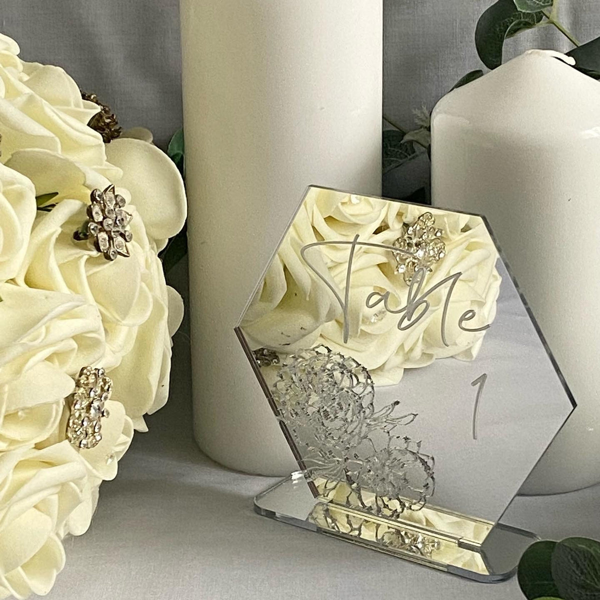 Engraved table number with floral design and 'Table 1' text, surrounded by white flowers and candles.