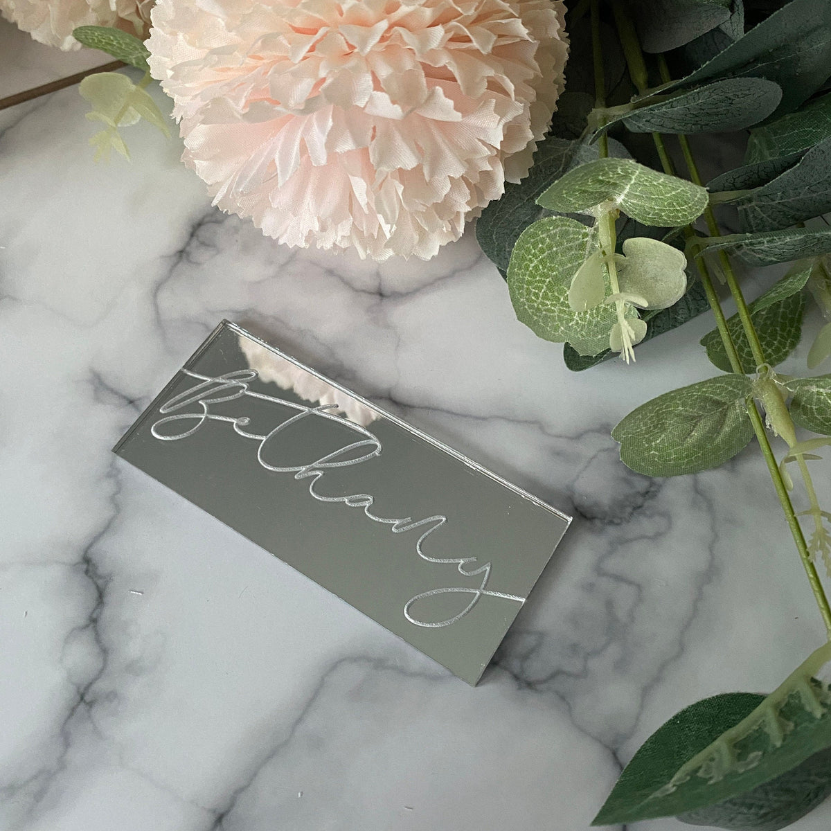 Engraved Wedding Place Name with 'Bethany' engraved in a script font on a marble surface with flowers and leaves.