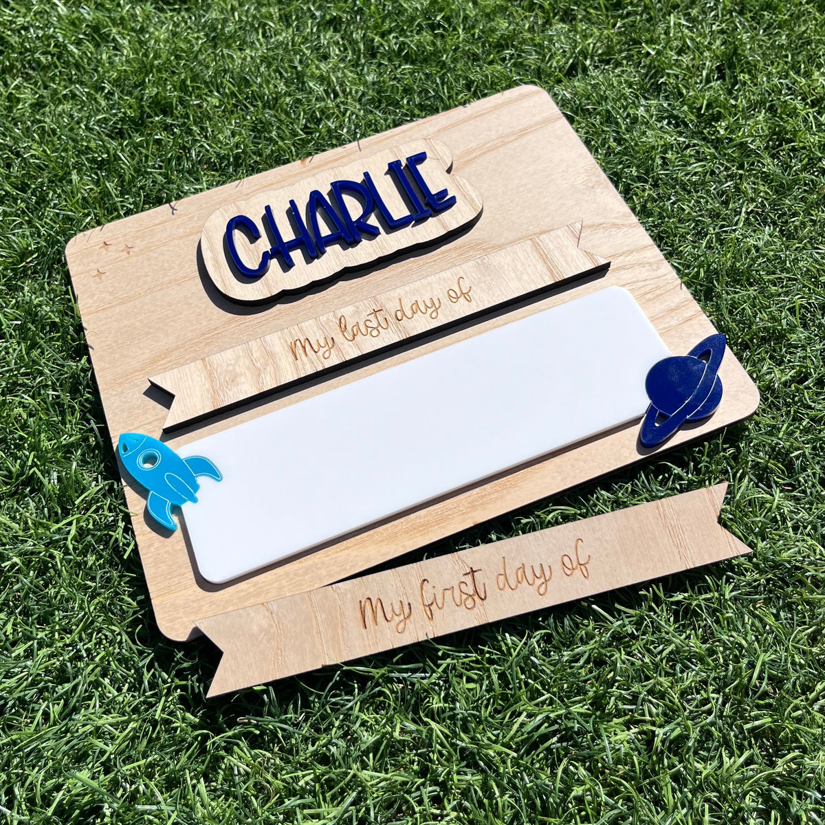 A personalised wooden first / last day sign with a white writing board, decorated with blue Rocket ship and planet.
