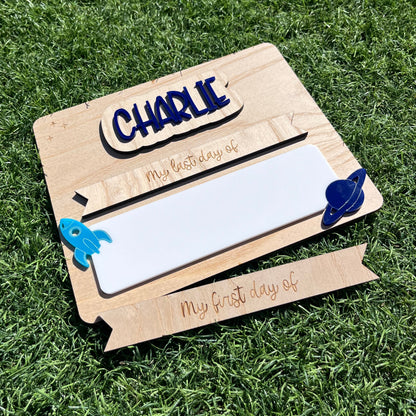A personalised wooden first / last day sign with a white writing board, decorated with blue Rocket ship and planet.