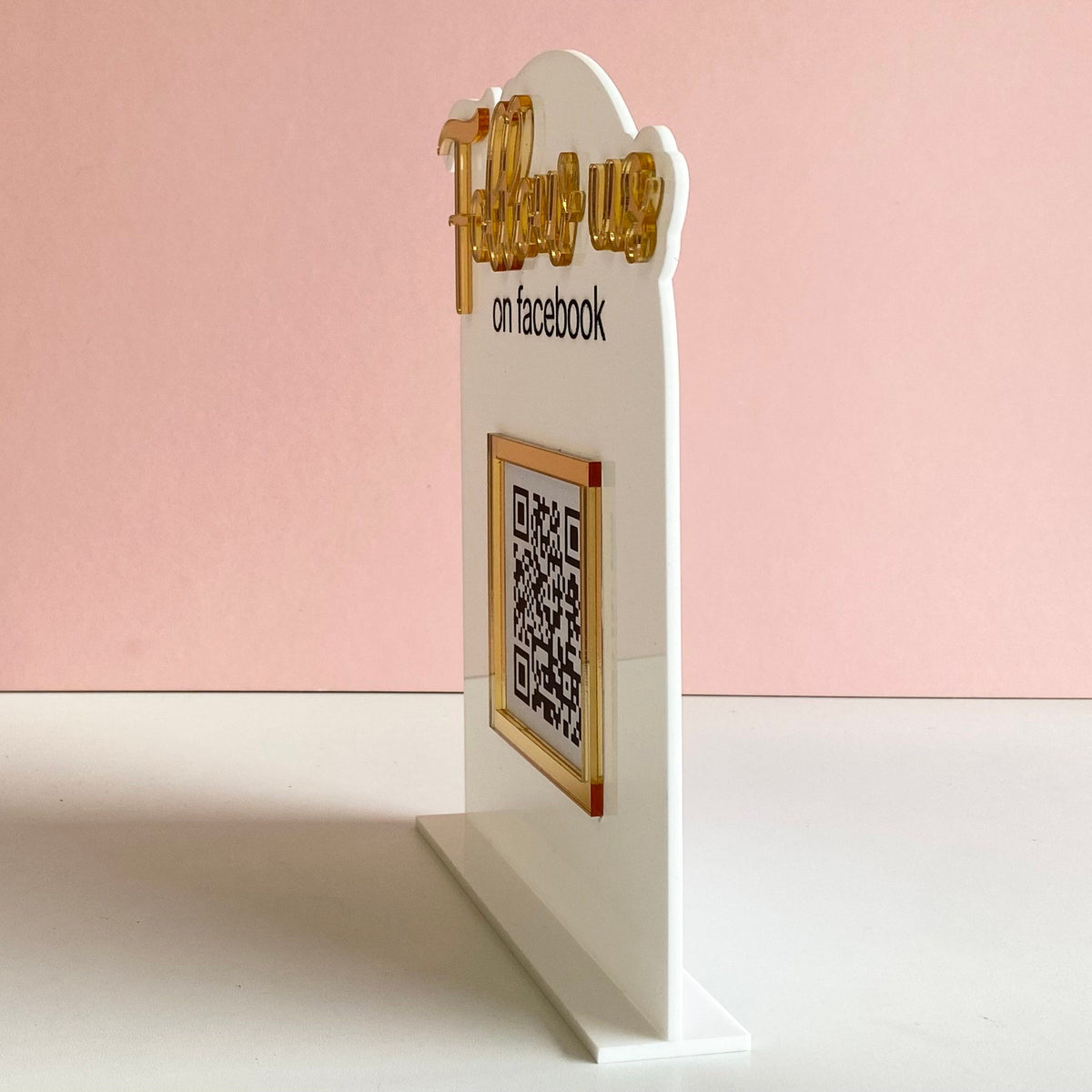 White stand with gold text and QR code on a pink background