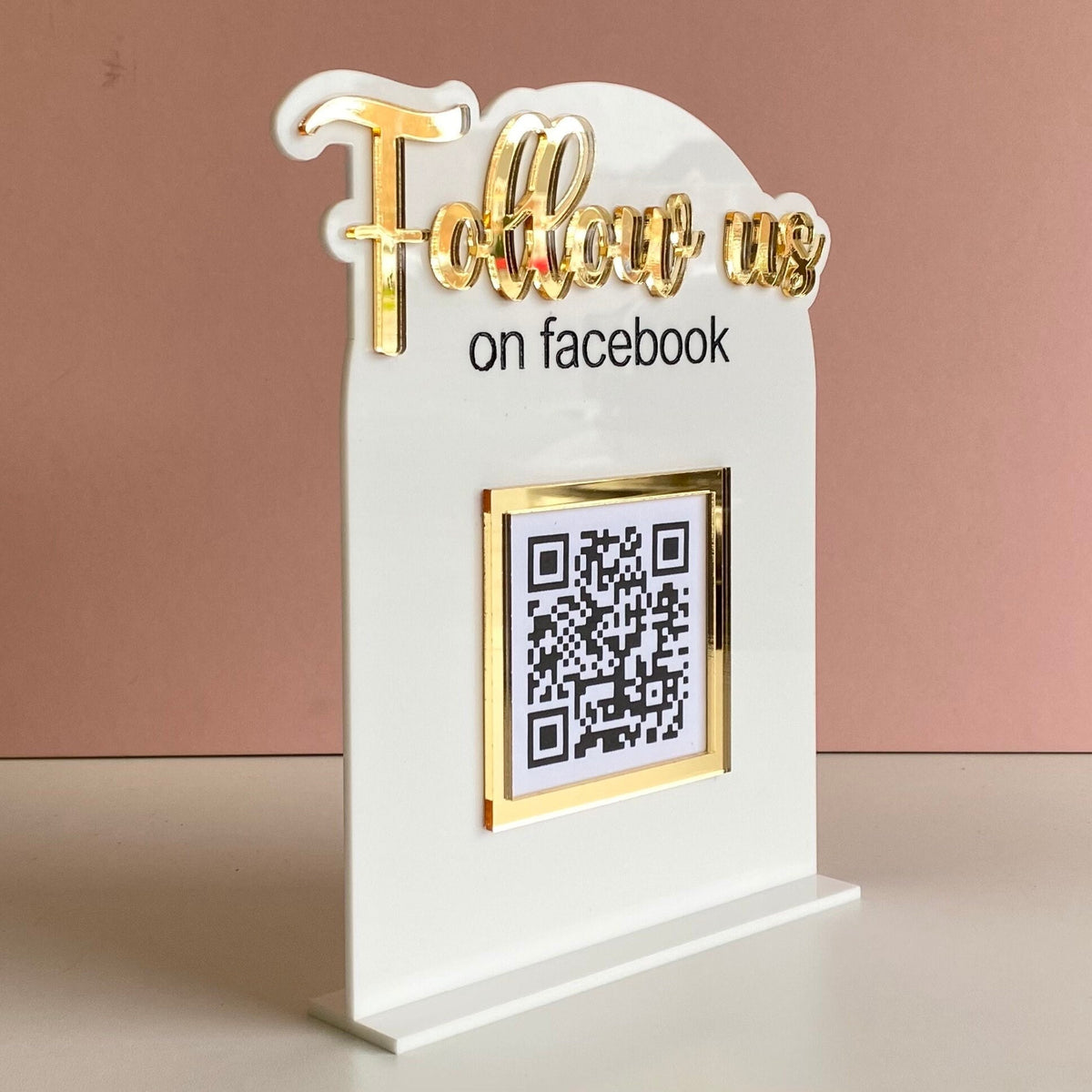 White and gold sign with 'Follow us on Facebook' text and QR code.