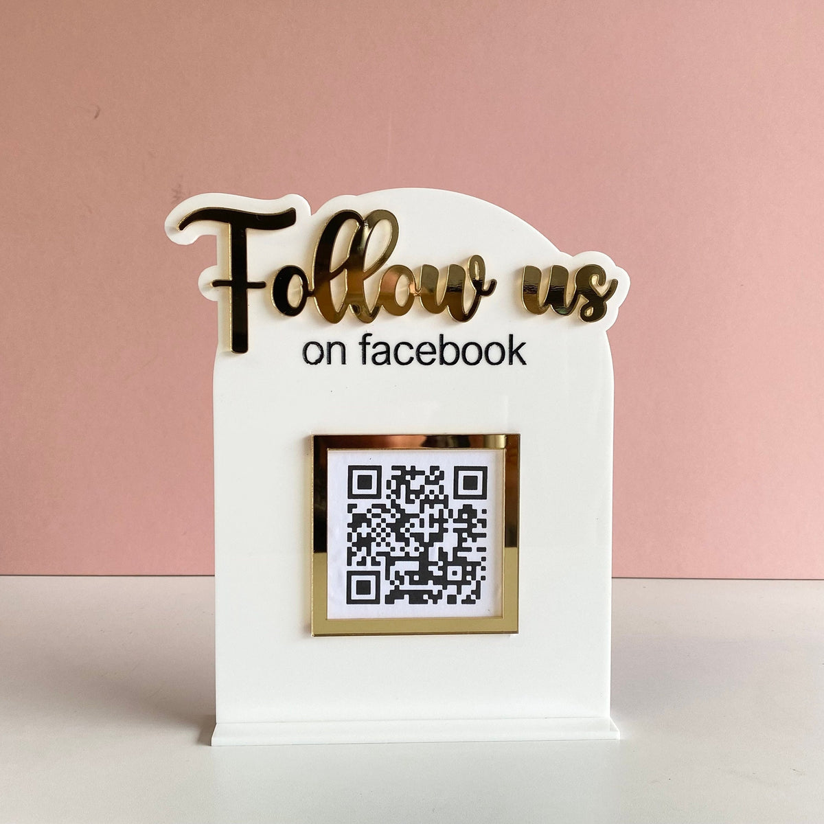 Decorative sign with 'Follow us on facebook' text and QR code on a pink background
