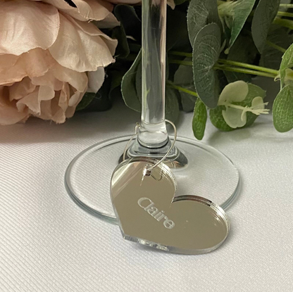 Heart-shaped name tag with 'Claire' on a wine glass stem, surrounded by flowers.