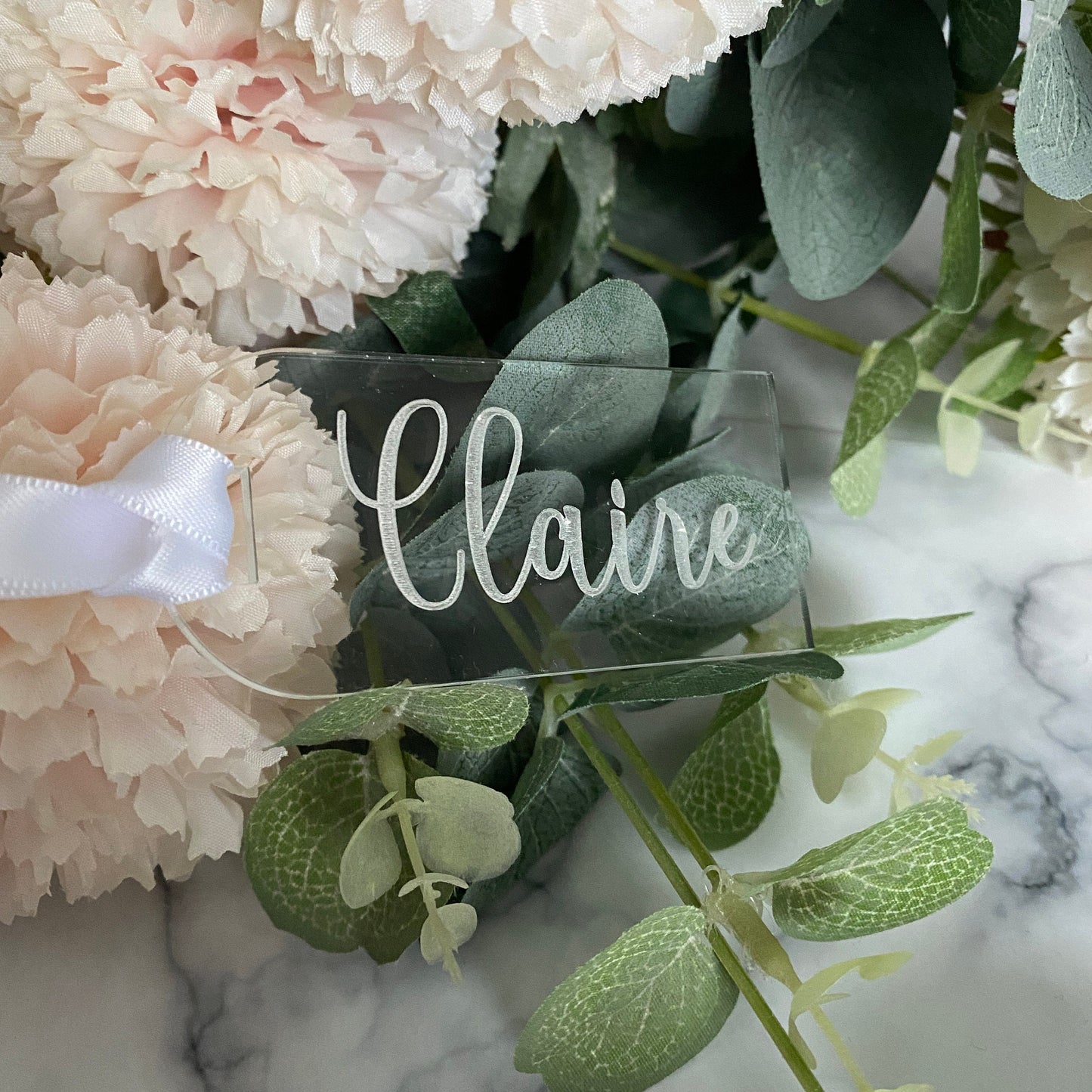 Clear acrylic Luxury Engraved Wedding Place Name with 'Claire' on a floral arrangement with pink and white flowers and green leaves.