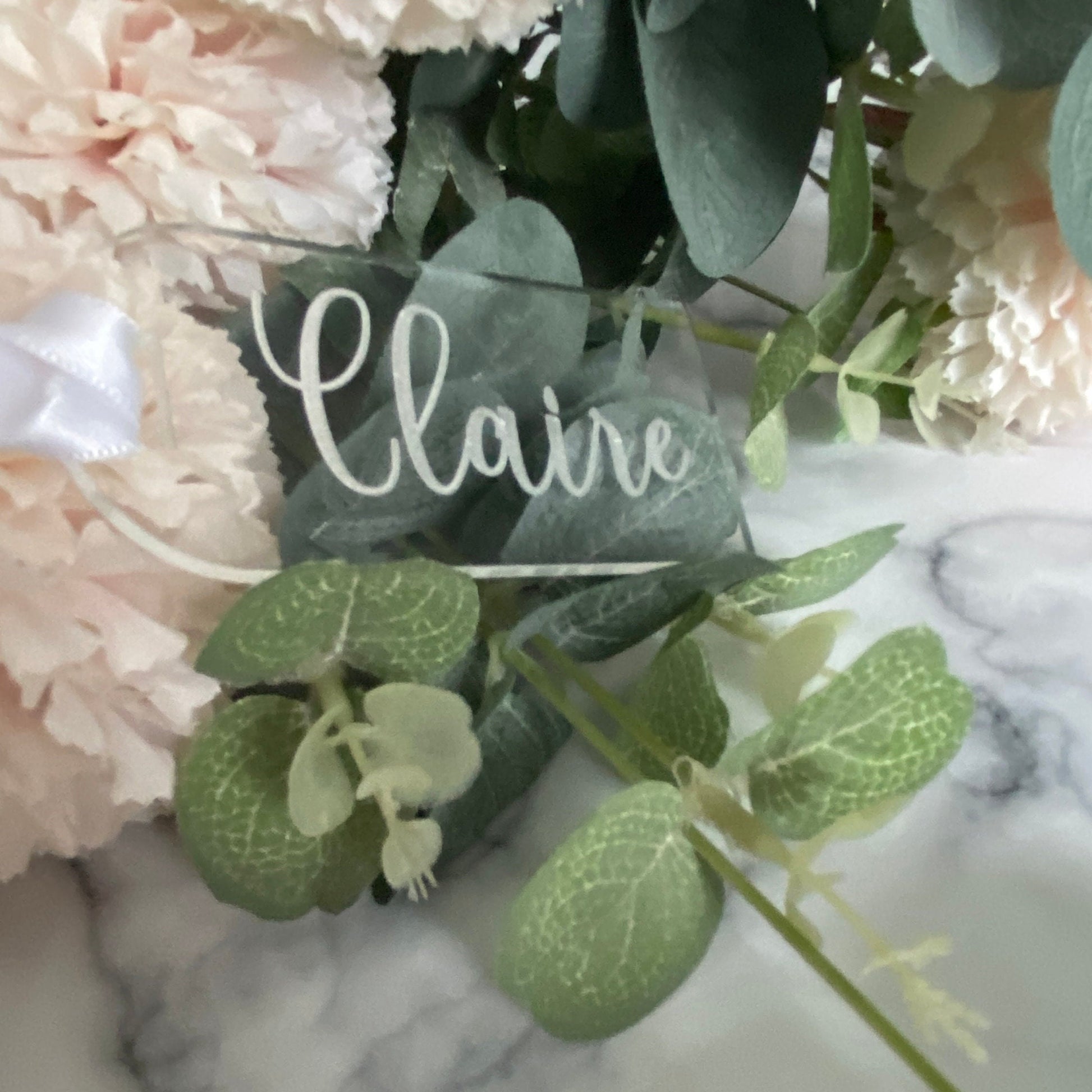 Bouquet of flowers with a decorative Luxury Engraved Wedding Place name card on a marble surface