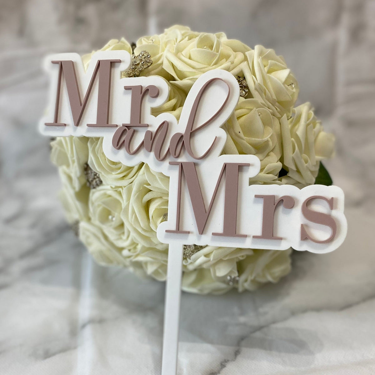 Decorative cake topper with 'Mr and Mrs' on a bouquet of white roses.