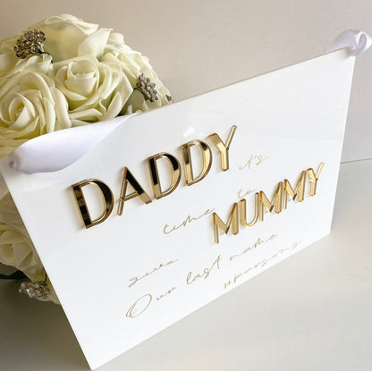 White acrylic sign with gold text saying Daddy it's time to give Mummy our last name'.
A sign perfect for any  page boy or flower girl 
