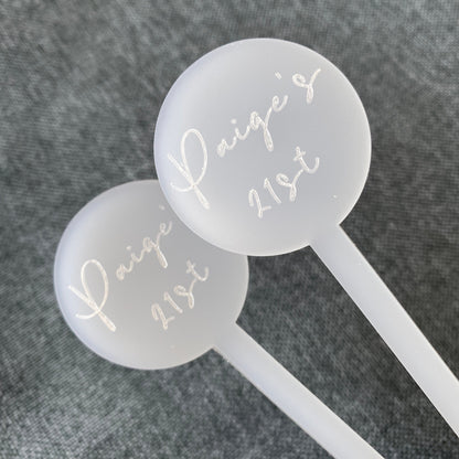 Two white cocktail stirrers with 'Paige's 21st' text on a gray background