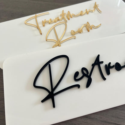 Two business signs with 'Treatment Room' and 'Restroom' text on a white acrylic base.