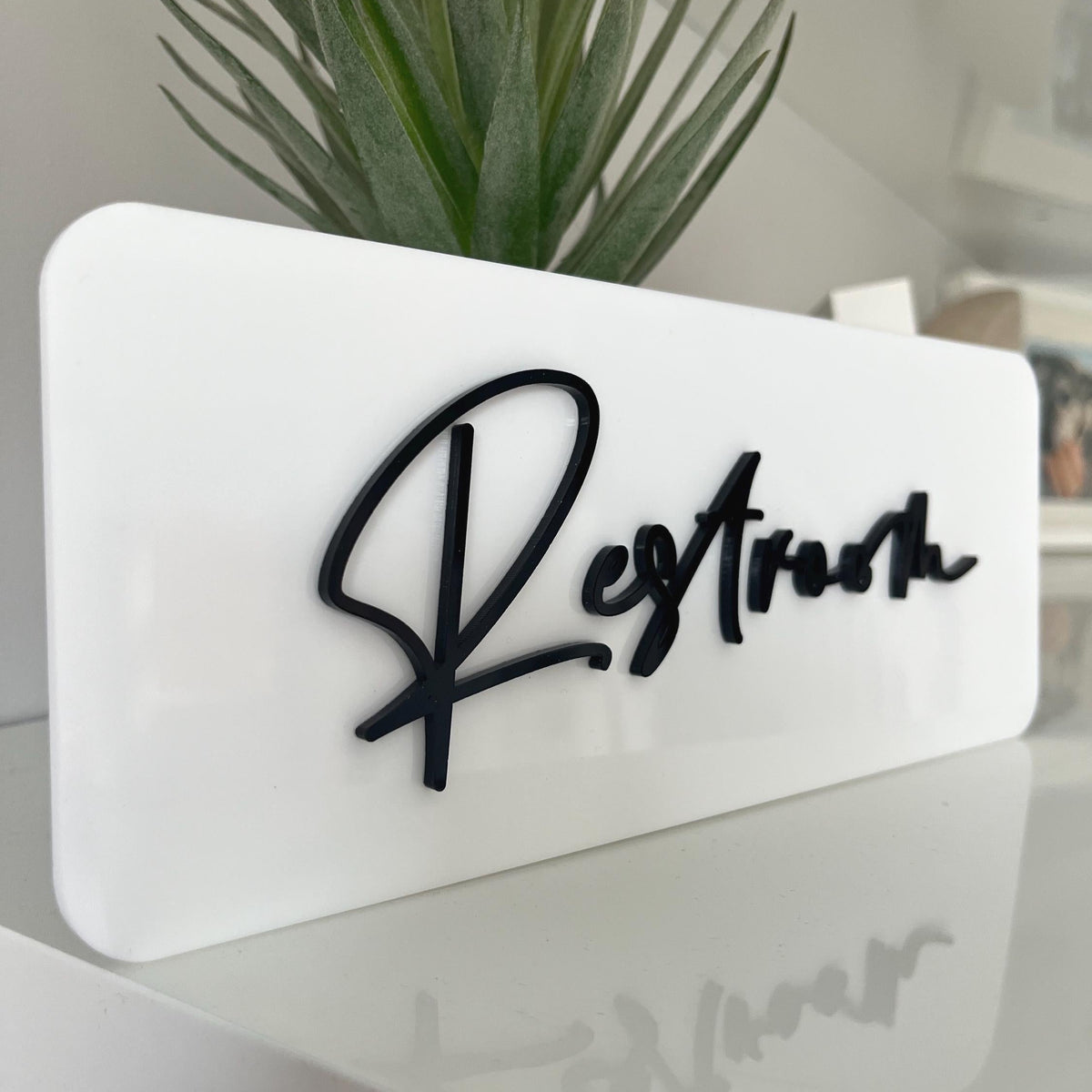 White acrylic business door sign with black 3d wording saying Restroom in a script style font