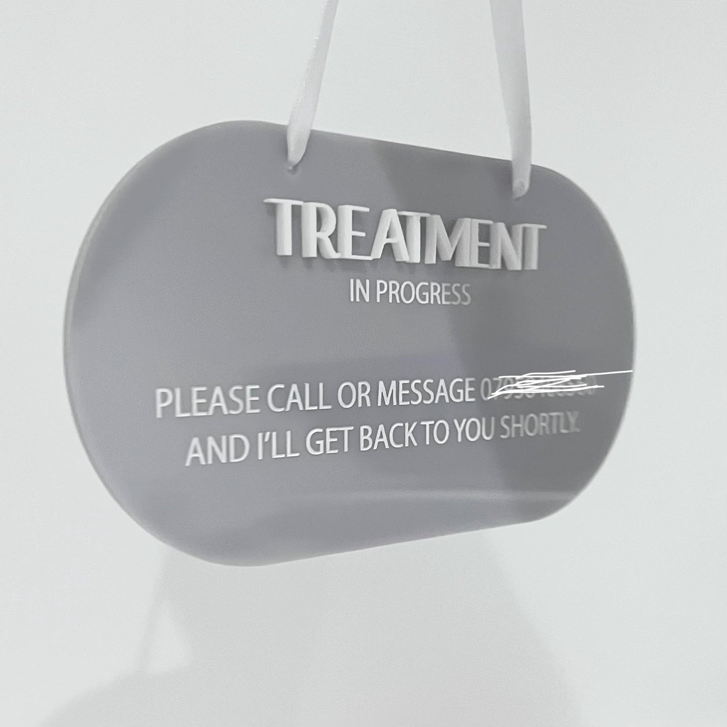 Grey acrylic sign with 'Treatment In Progress' message on a white background