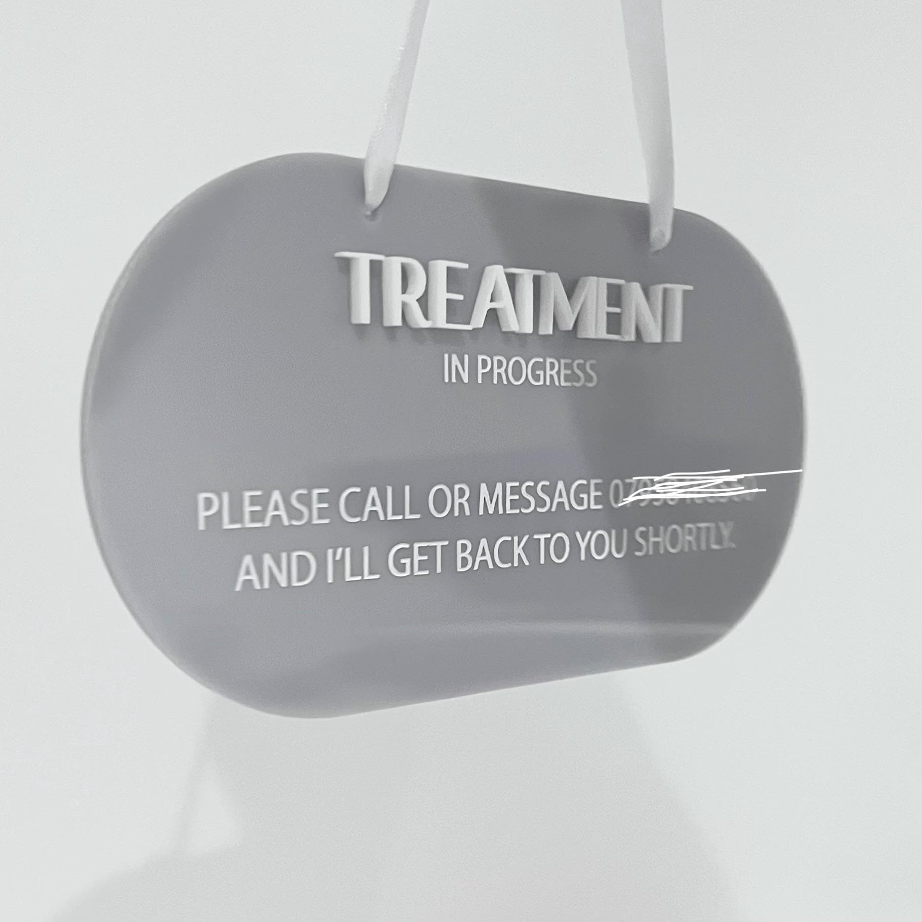 Grey acrylic sign with 'Treatment In Progress' message on a white background