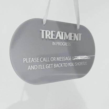 Grey acrylic sign with 'Treatment In Progress' message on a white background