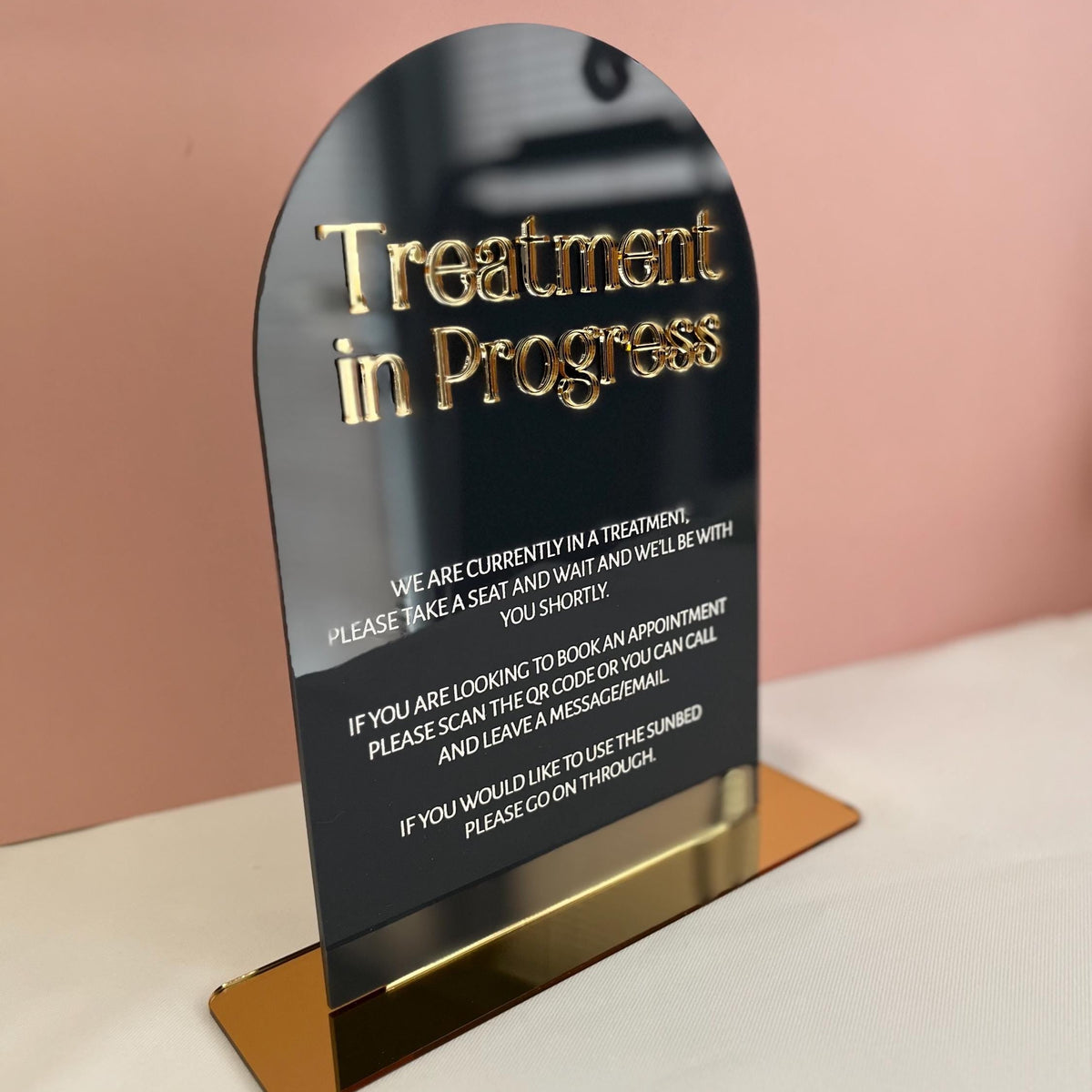 Sign indicating 'Treatment in Progress' with gold text on a black background, placed on a stand against a pink wall.