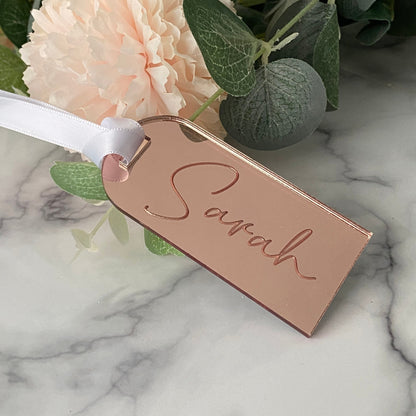 Rose gold Wedding Place Name with 'Sarah' engraved, ribbon, and flowers on marble background