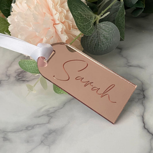 Rose gold Wedding Place Name with 'Sarah' engraved, ribbon, and flowers on marble background