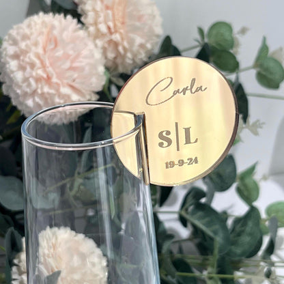 Gold  mirror acrylic round Wedding Place Setting Glass Charms with 'Carla S/L' and '19-9-24' on a clear glass with flowers in the background
