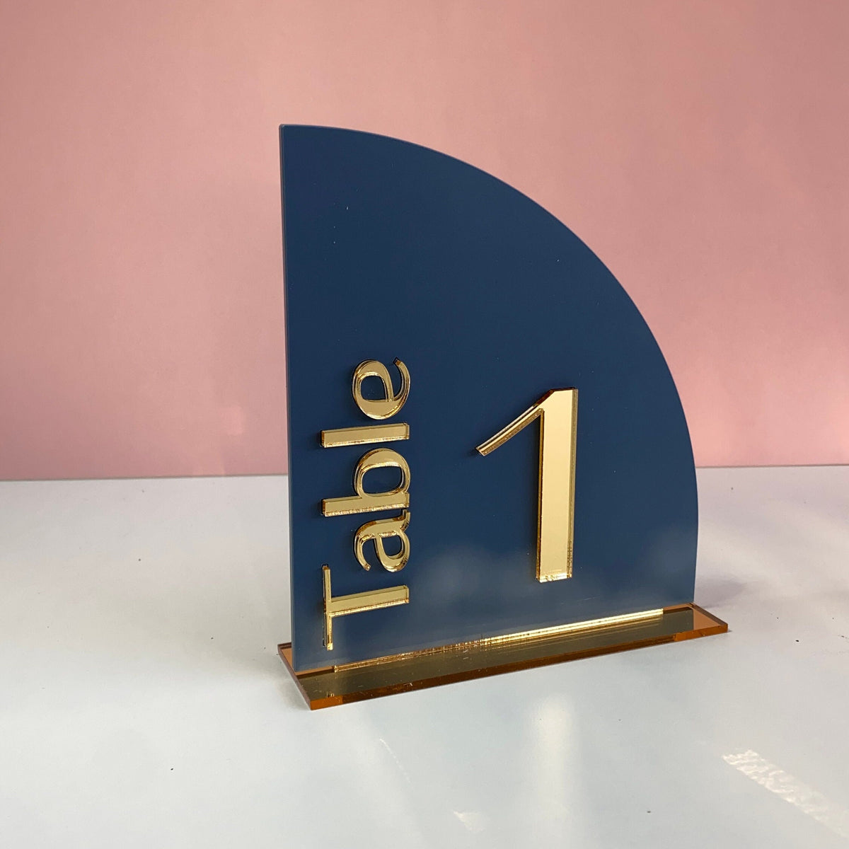Blue table number holder with gold 'Table 1' text on a pink background