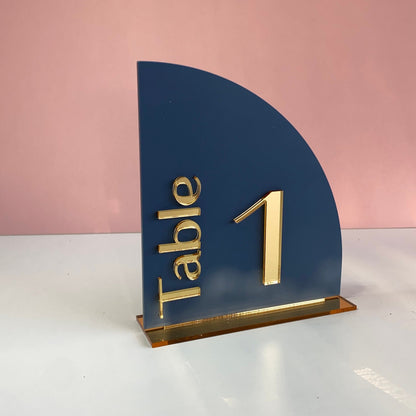 Blue table number holder with gold 'Table 1' text on a pink background
