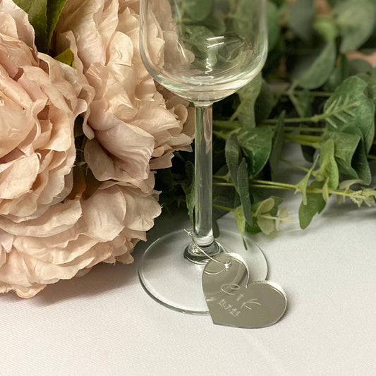 Wine glass with heart-shaped tags on a white surface with flowers and greenery.