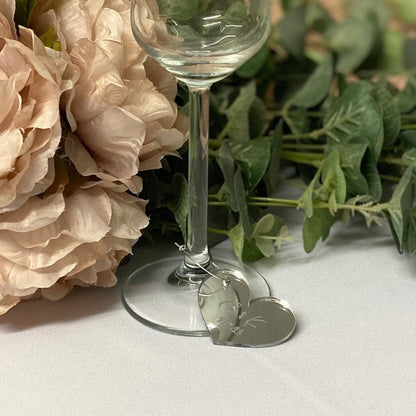 Clear glass with heart charm  wedding place name on a white surface with flowers and greenery
