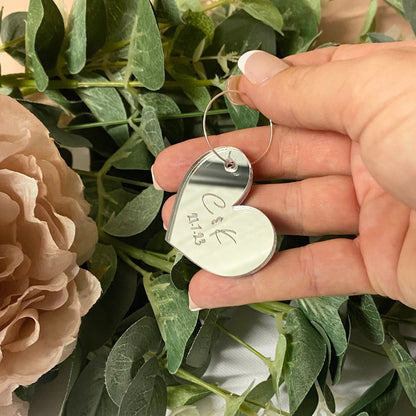 Heart-shaped silver drinks tag with engraved text held over a bouquet of flowers.